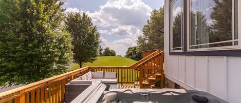 A hot tub on a deck with a wooden railing, a staircase, and a view of a green landscape.