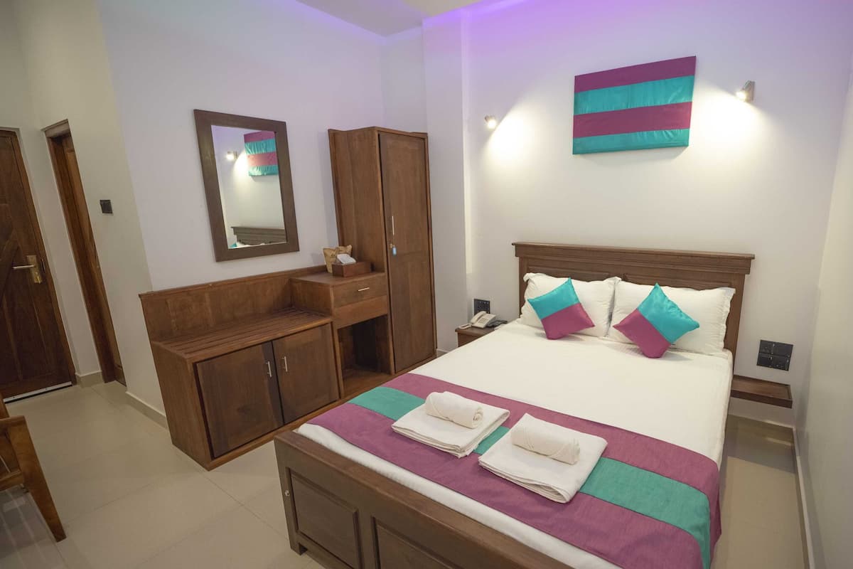 A hotel room with a bed, a wooden wardrobe, a bedside table with a phone, and a wall-mounted light.