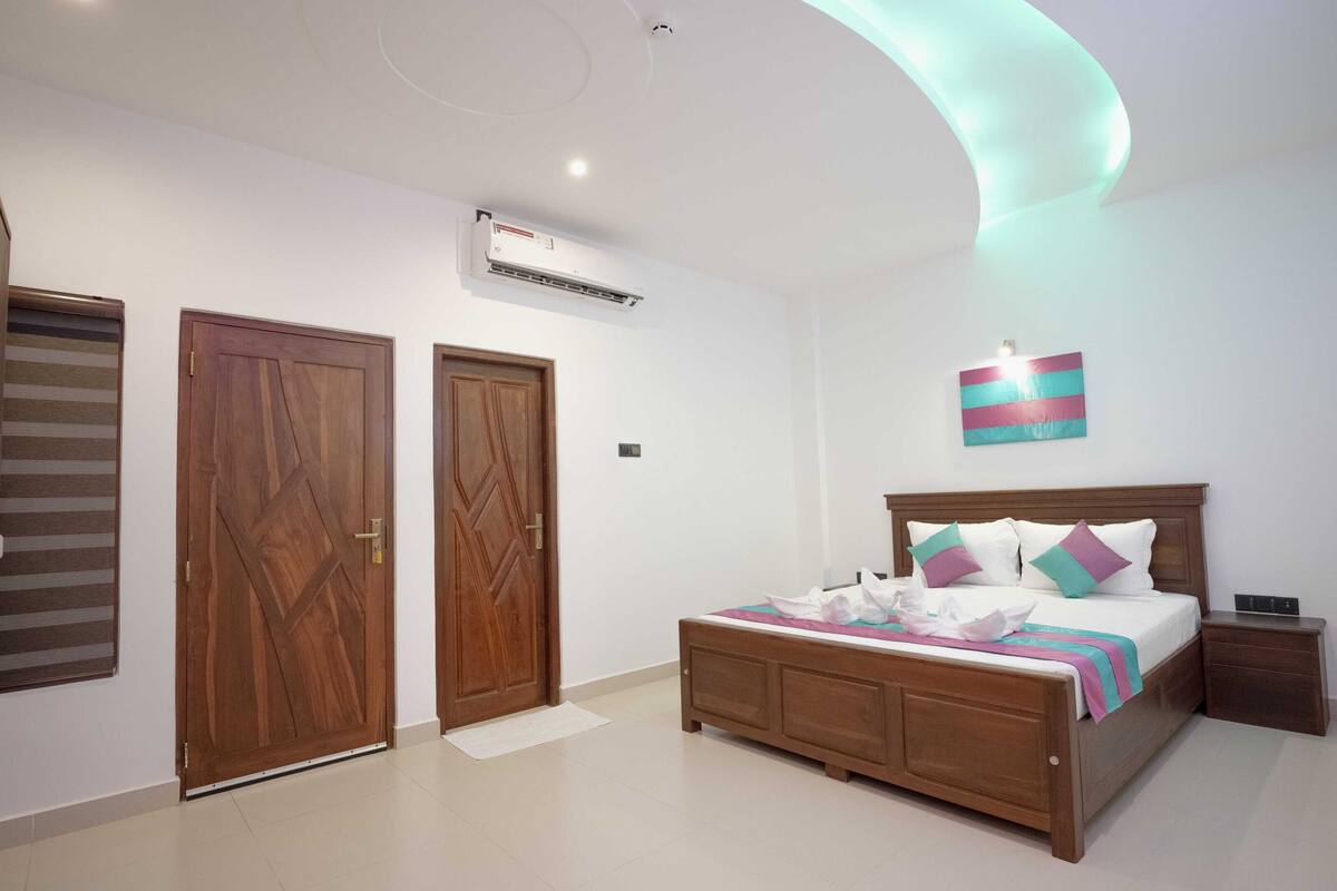 A bedroom with a wooden bed, two doors, an air conditioning unit, and a ceiling light.