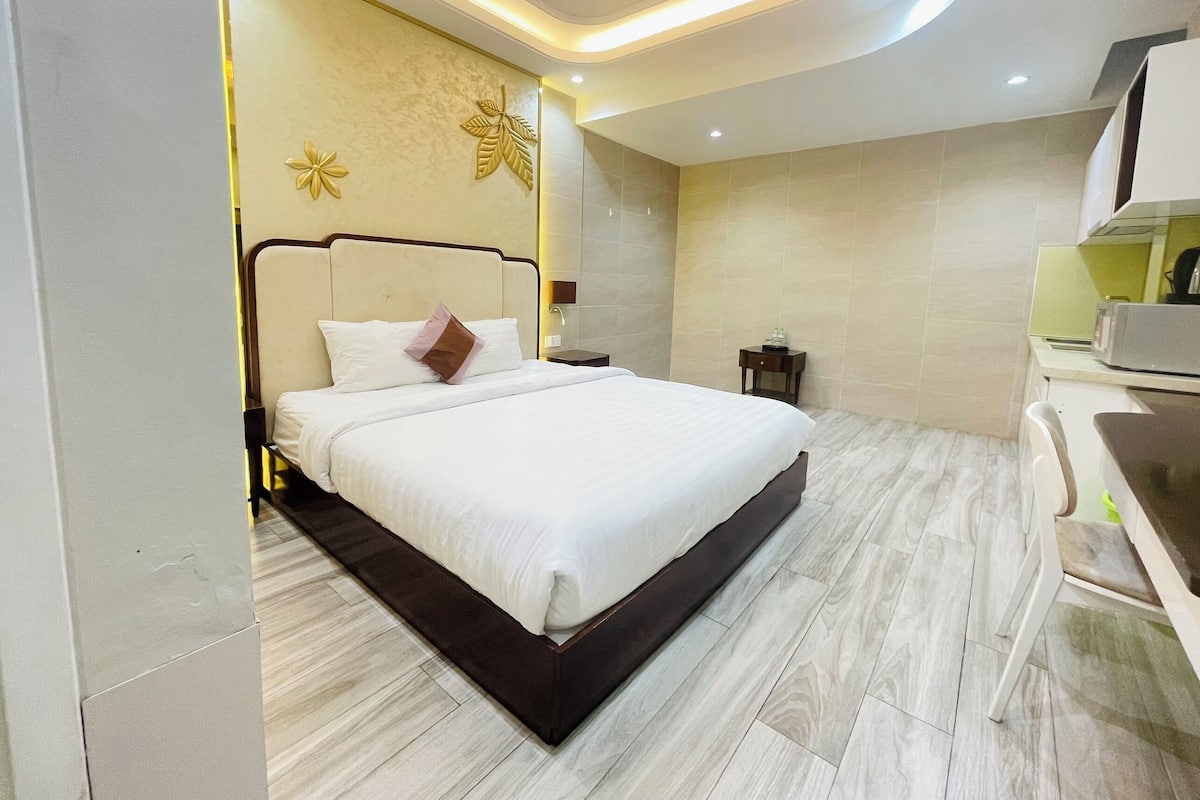 Quarto de hotel moderno com uma cama grande, uma pequena mesa de cabeceira e uma escrivaninha embutida com micro-ondas.