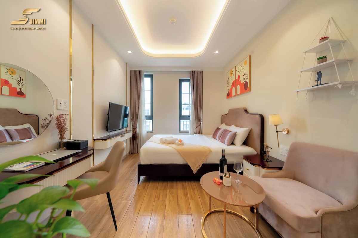 Quarto de hotel moderno com cama, escrivaninha, cadeira, sofá, televisão e uma pequena mesa com garrafa e copo.