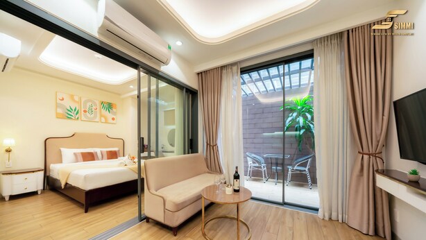 A hotel room with a bed, a sofa, a small table with a bottle and glasses, and a TV on the wall.