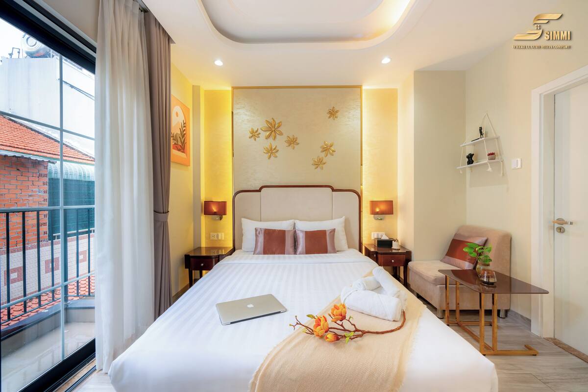 Quarto de hotel com cama, um laptop, toalha e uma pequena mesa com uma planta.