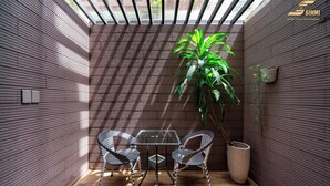A modern patio with a glass table and metal chairs, surrounded by wooden walls and a large potted plant.