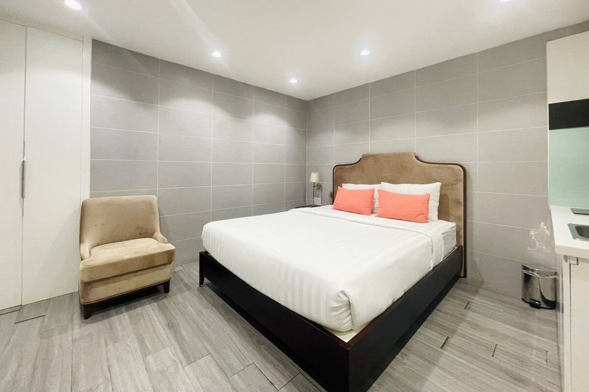 Quarto de hotel moderno com uma cama, uma poltrona e uma pequena mesa.
