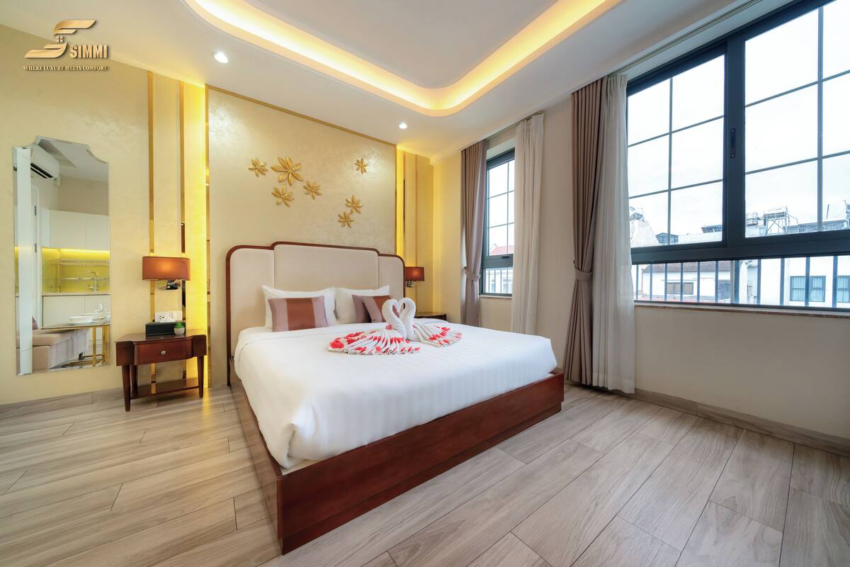 Quarto de hotel com uma cama grande, mesas de cabeceira, um espelho e vista da cidade através de grandes janelas.