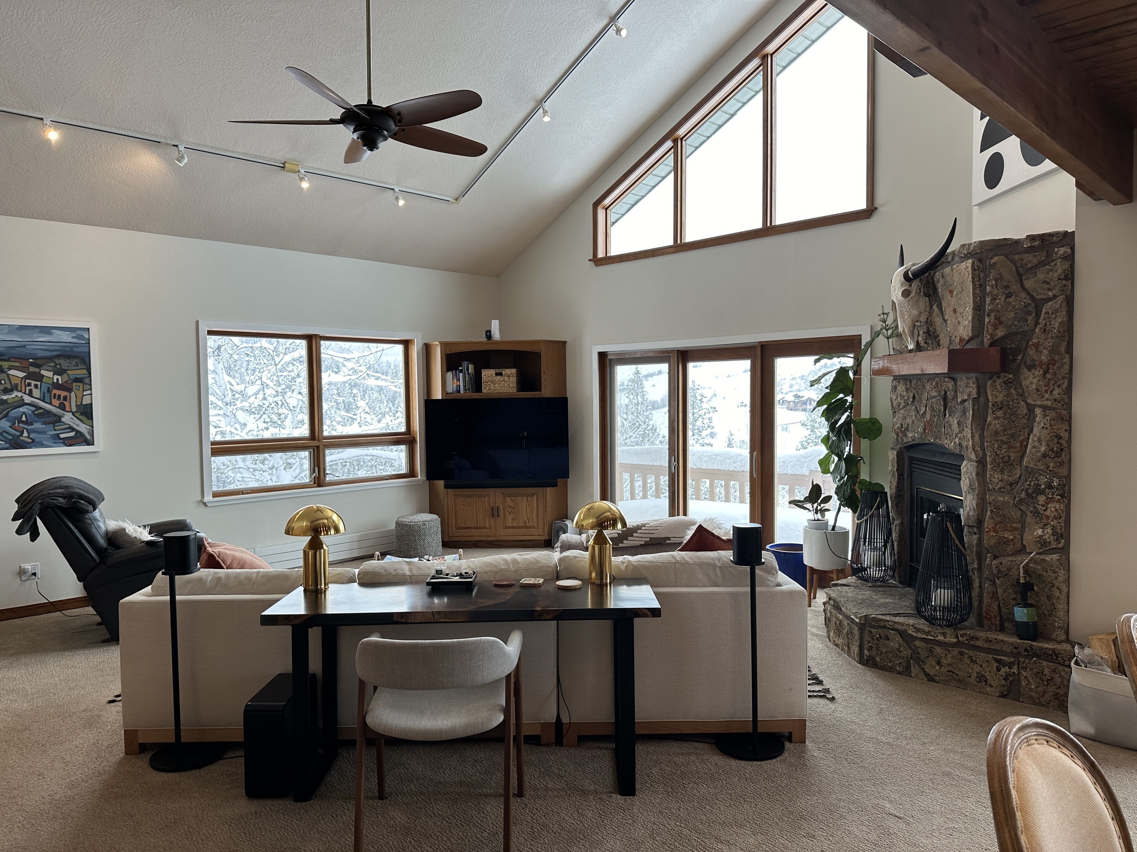 A spacious living room with a high ceiling, large windows, a fireplace, and a cozy seating area.
