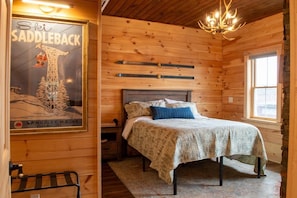 Interno di una baita in legno con un letto, un poster e un lampadario.