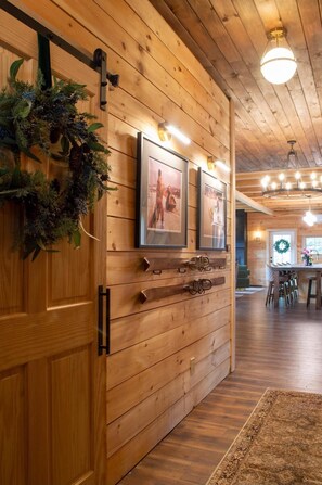 A wooden interior with a door, wall-mounted lights, framed pictures, and a chandelier.