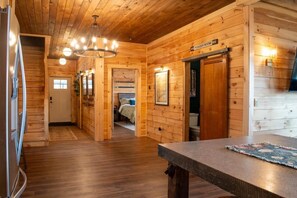 A wooden cabin interior with a kitchen, dining area, and a bedroom.