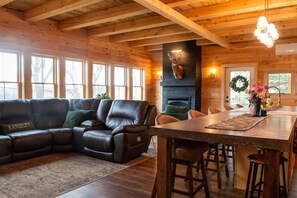 A wooden interior with a fireplace, leather sofa, dining table, and bar stools.