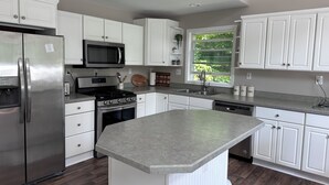 A modern kitchen with white cabinetry, stainless steel appliances, a granite countertop, and a window providing natural light. - Spacious home, 12 miles from Nubs Nob, Harbor Springs surrounded by forest. (Alanson)