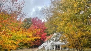 A house with a white exterior and a red roof, surrounded by trees with autumn foliage. - Spacious home, 12 miles from Nubs Nob, Harbor Springs surrounded by forest. (Alanson)