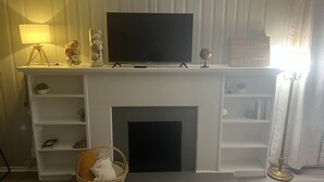 Una sala de estar con chimenea, un televisor sobre una repisa y una lámpara.