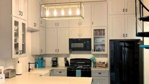 Una cucina moderna con mobili bianchi, un frigorifero nero, un forno a microonde e un'isola centrale con sgabelli.