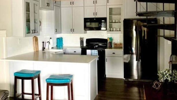 Una cucina moderna con mobili bianchi, un'isola centrale con sgabelli, un frigorifero in acciaio inossidabile e una lampada a sospensione.
