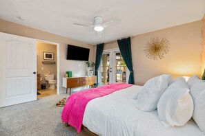 A bedroom with a bed, a ceiling fan, a TV, and a bathroom visible through an open door. - Casita Cerritos  (Palm Springs)