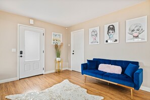 A room with a blue sofa, a white door, and framed pictures on the wall. - Casita Cerritos  (Palm Springs)