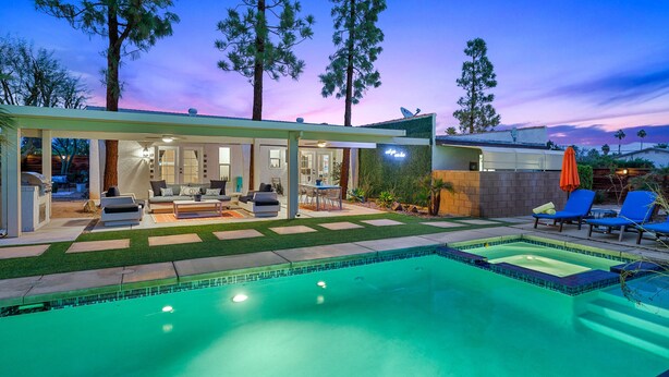 Ein moderner Poolbereich im Freien mit einer Terrasse, Liegestühlen und einer überdachten Sitzecke.