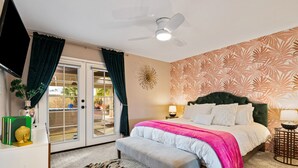 Ein Schlafzimmer mit einem Bett, einem Deckenventilator, einem Fenster mit Vorhängen, einem Nachttisch, einer Lampe und einem Teppich mit Tigerprint.