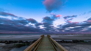Een houten looppad dat naar een strand leidt, met een bewolkte lucht.