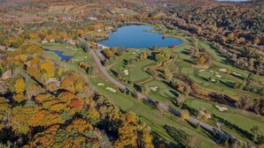 A golf course with a lake, surrounded by autumn-colored trees and rolling hills. - Luxe Mountainside Home with Panoramic Valley Views (Quechee)