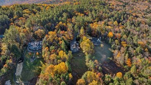 A large estate with multiple houses surrounded by dense forest. - Luxe Mountainside Home with Panoramic Valley Views (Quechee)