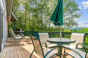 Eine Holzterrasse mit Gartenmöbeln, einem Grill und Blick auf einen bewaldeten Bereich.