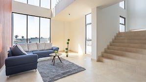 A spacious living area with a blue sofa, a small round coffee table, and a gray rug. There is a staircase to the right and large windows providing natural light. - WinDay Veracruz Hotel Express (Veracruz)