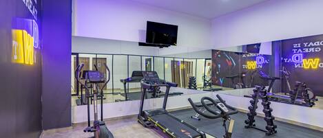 Un gimnasio con equipamiento de ejercicio, una televisión y carteles motivacionales.