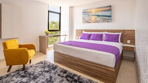 A modern bedroom with a large bed, a yellow armchair, a view of the outdoors, and a painting of a sunset. - WinDay Veracruz Hotel Express (Veracruz)