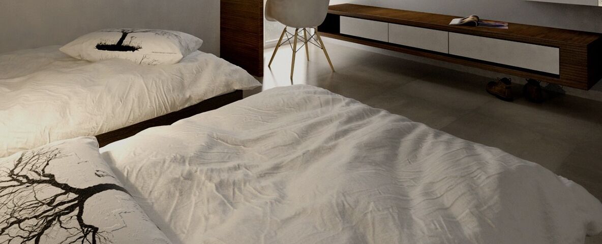 Two beds with white linens, a wooden bedside table, and a white chair.