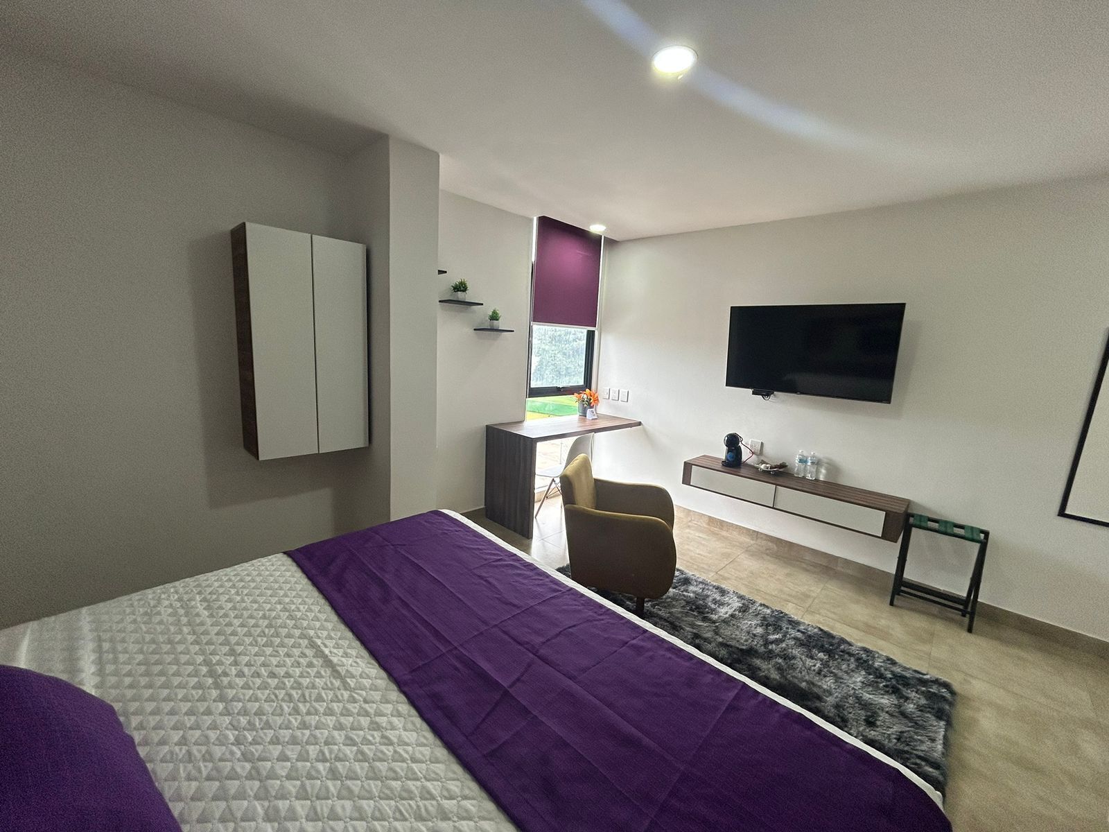A modern bedroom with a bed, a desk, a chair, a TV, and a wardrobe.
