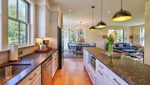 A modern kitchen with a central island, a dining area with a chandelier, and a living room with a blue sofa and a coffee table. - Picturesque Farmhouse Retreat Minutes from Stowe (Morrisville)