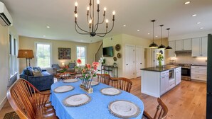 A spacious kitchen with modern appliances, a dining area with a blue tablecloth and wooden chairs, and a cozy living room with a sofa and a lamp. - Picturesque Farmhouse Retreat Minutes from Stowe (Morrisville)