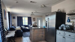 Een kleine keuken met een koelkast, spoelbak en een zithoek met een bank en stoelen.