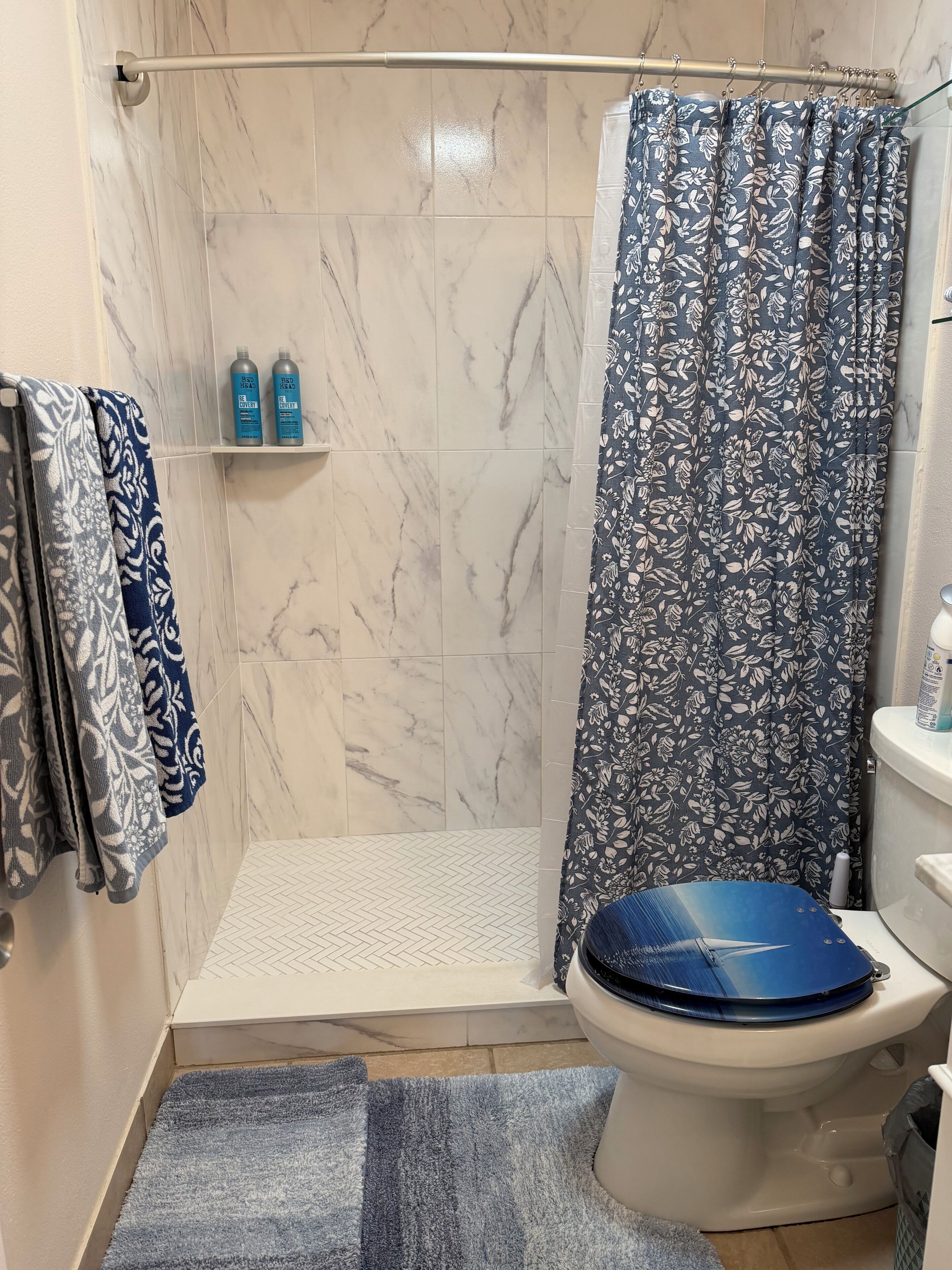A bathroom with a shower, toilet, and a towel rack with patterned towels.