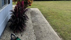 Een woonhuis met een verzorgd gazon, een bloembed met kleurrijke bloemen en een betonnen pad naar de woning.