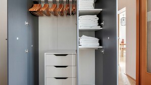 Une salle de bain moderne aux tons de gris et de blanc, dotée d’une douche intégrée, d’un meuble-lavabo blanc avec des tiroirs et d’un porte-serviettes avec des poignées en bois.