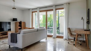 Un salon moderne avec un canapé, un téléviseur et un balcon équipé de chaises.