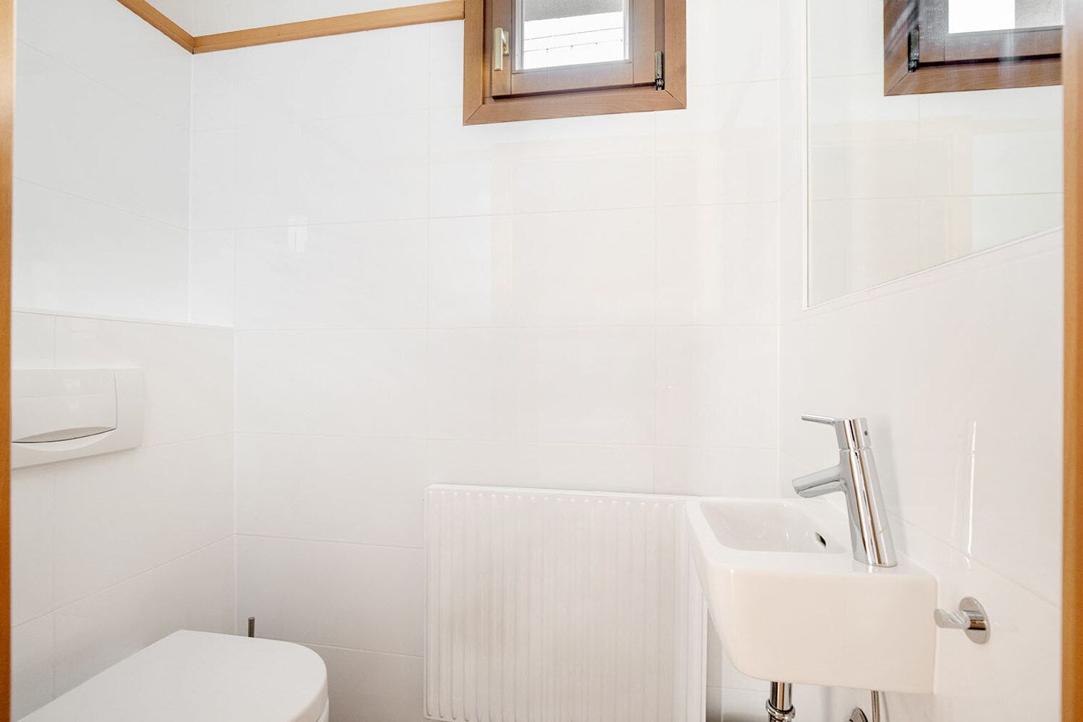 Une salle de bain moderne avec des carreaux blancs, des toilettes, un lavabo et une fenêtre.