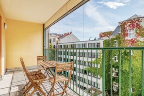 Un balcón con una mesa y sillas, vistas a edificios y una barandilla de metal verde.