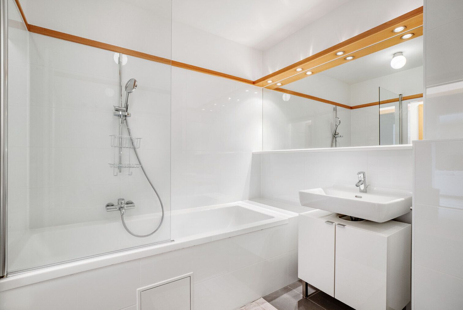 Un baño moderno con una ducha envuelta en vidrio, un lavabo blanco y un espejo grande.