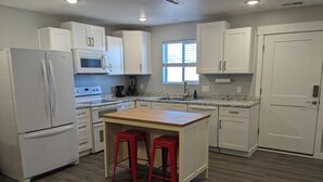 A kitchen with white cabinets, a refrigerator, a microwave, a coffee maker, and a window.