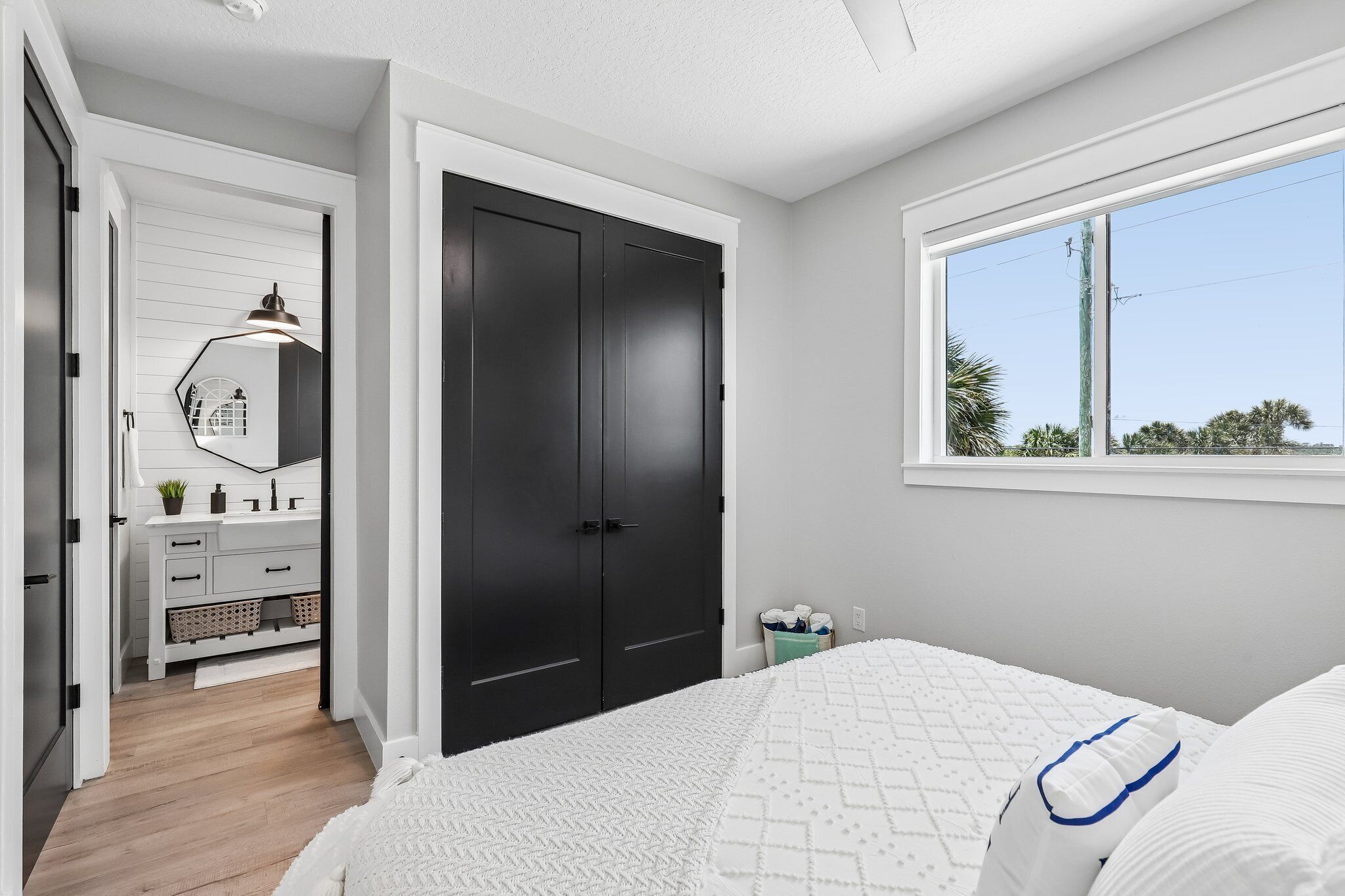 A bedroom with a bed, a window, a wardrobe, and a bathroom with a mirror and sink.