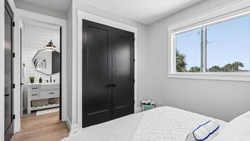 A bedroom with a bed, a window, a wardrobe, and a bathroom with a mirror and sink.