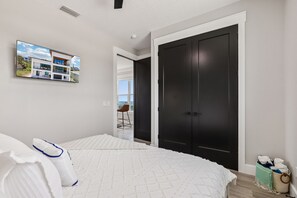 Una camera da letto con un letto, una TV a muro, una porta scura e una finestra.