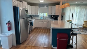 A modern kitchen with white cabinets, a stainless steel refrigerator, a built-in oven, and a coffee maker. There's a red trash bin and a broom near the sink. - Private one level home with pool near Anna Maria Island (Bradenton)