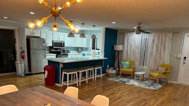A modern kitchen with white cabinets, a central island, and a dining area with a wooden table and chairs. - Private one level home with pool near Anna Maria Island (Bradenton)