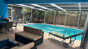 A covered outdoor area with a swimming pool, lounge chairs, and a table with chairs. - Private one level home with pool near Anna Maria Island (Bradenton)